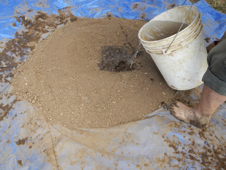 Our cob recipe is 1 part local soil, 1 part sand and 1/4 part clay (high-clay soil). We place it all on the tarp and gradually add water.