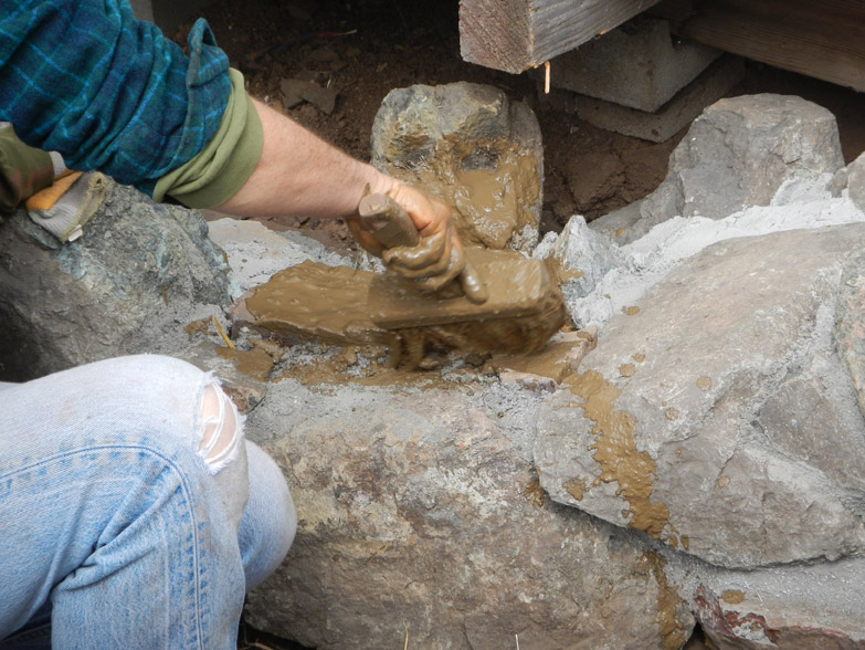 Before putting cob in the rocks, we pre-wet the surface with "slip" - a thin water and clay mix. It helps the cob stick to the stone.